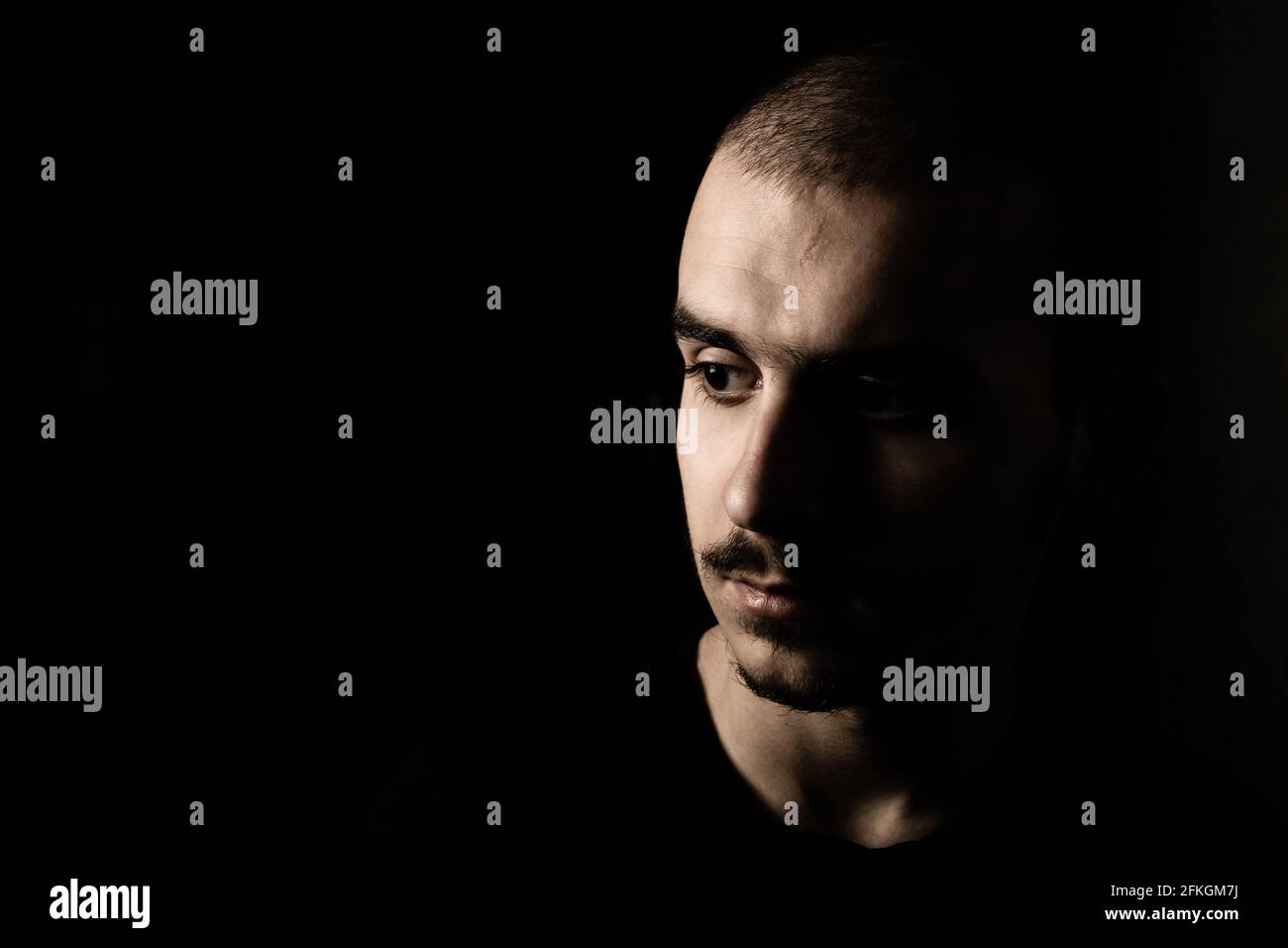 Portrait d'un jeune homme avec moustache isolé sur fond noir et foncé. Banque D'Images
