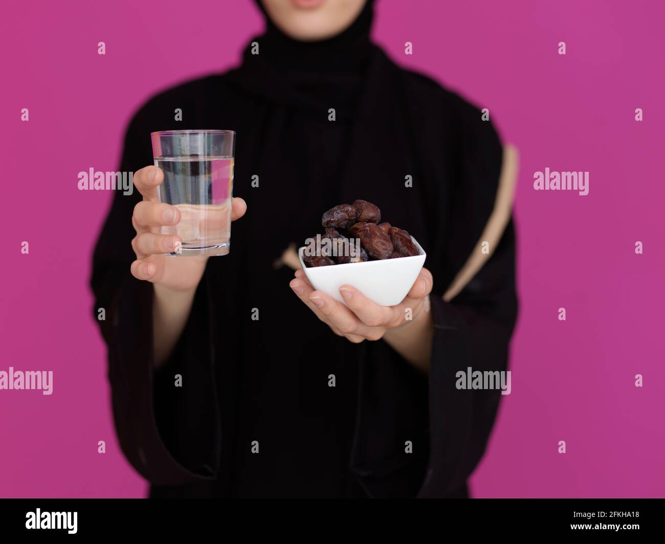 Femme musulmane moderne en abaya tenant un fruit dattier et un verre d'eau devant elle. Concept célébration de l'heure de l'iftar, fin du jeûne, dans le ramadan ho Banque D'Images