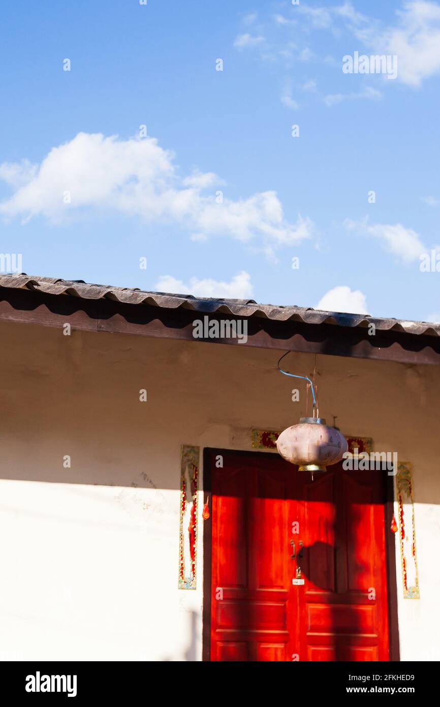 Lever de soleil brillant sur une ancienne maison du Yunnanese, porte rouge contre le mur blanc et ciel bleu dans les fonds. Doi Mae Salong, Chiang Rai, Thaïlande. Banque D'Images Lever de soleil brillant sur une ancienne maison du Yunnanese, porte rouge contre le mur blanc et ciel bleu dans les fonds. Doi Mae Salong, Chiang Rai, Thaïlande. Banque D'Images