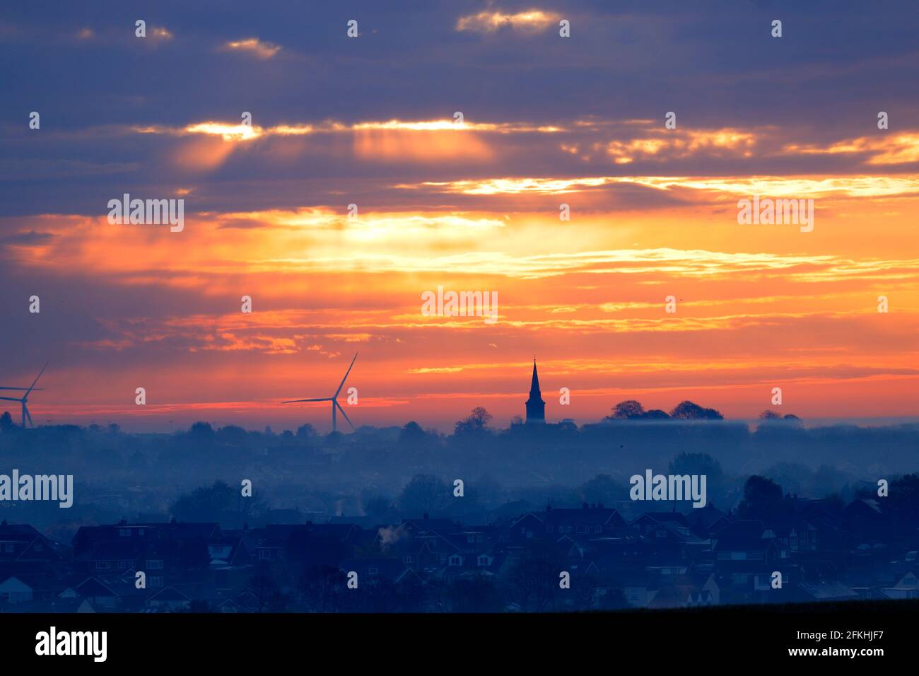 Lever de soleil sur Garforth à Leeds. L'église Sainte-Marie se dresse au-dessus des toits avec des éoliennes de Hook Moor. Banque D'Images