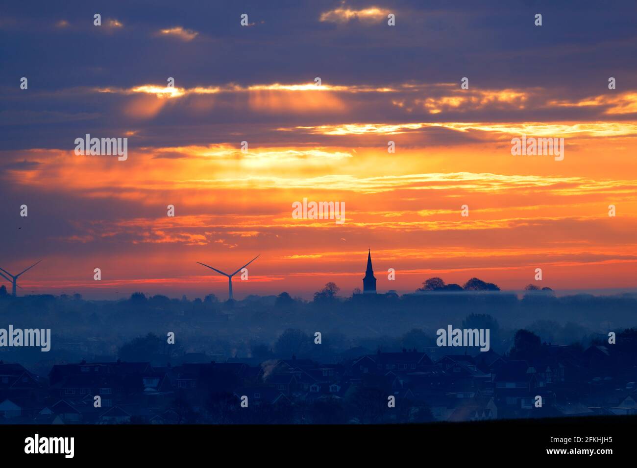 Lever de soleil sur Garforth à Leeds. L'église Sainte-Marie se dresse au-dessus des toits avec des éoliennes de Hook Moor. Banque D'Images