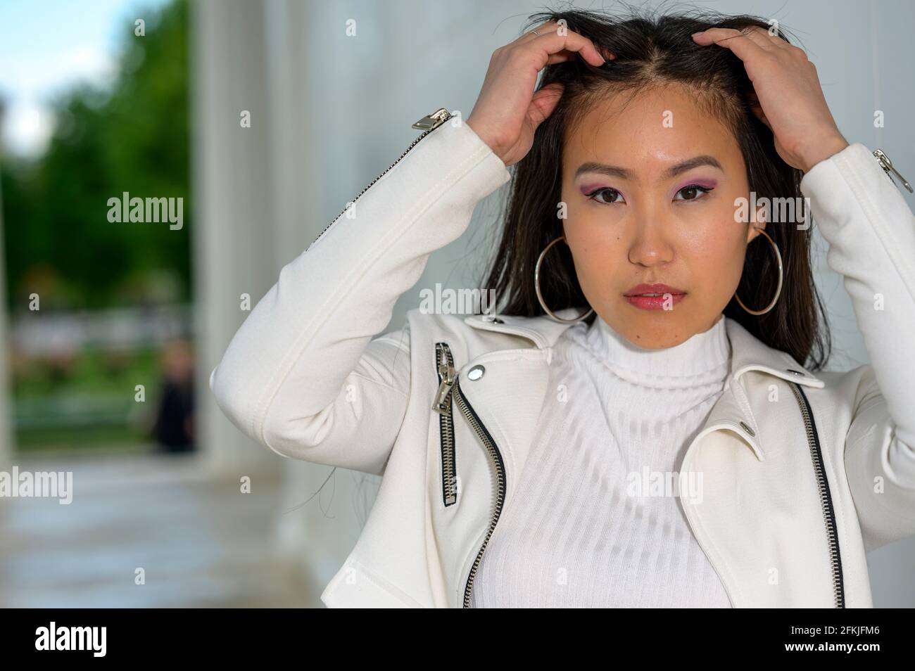 Une jeune femme mongole avec une veste en cuir blanc dans un parc urbain. Banque D'Images