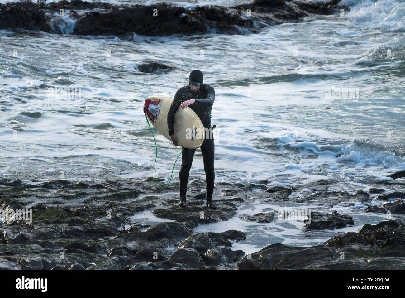 Un surfeur transportant sa planche de surf et marchant hors de la mer à Little Fistral à Newquay en Cornouailles. Banque D'Images