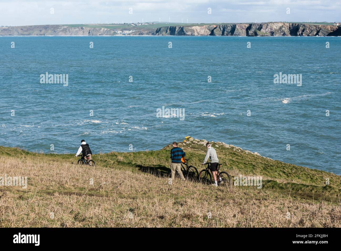 Trois jeunes hommes poussent des bicyclettes le long d'un sentier sur Towan Head, surplombant la baie de Newquay, dans les Cornouailles. Banque D'Images