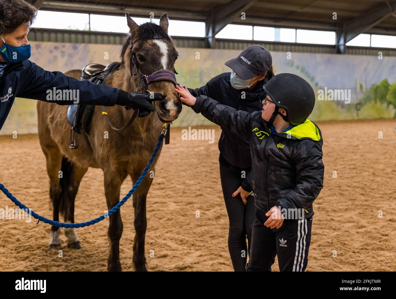 Garçon avec le syndrome de Down patrouiller le cheval avec sa mère portant un masque facial à Riding for Disabled, Muirfield Riding Therapy, East Lothian, Écosse, Royaume-Uni Banque D'Images