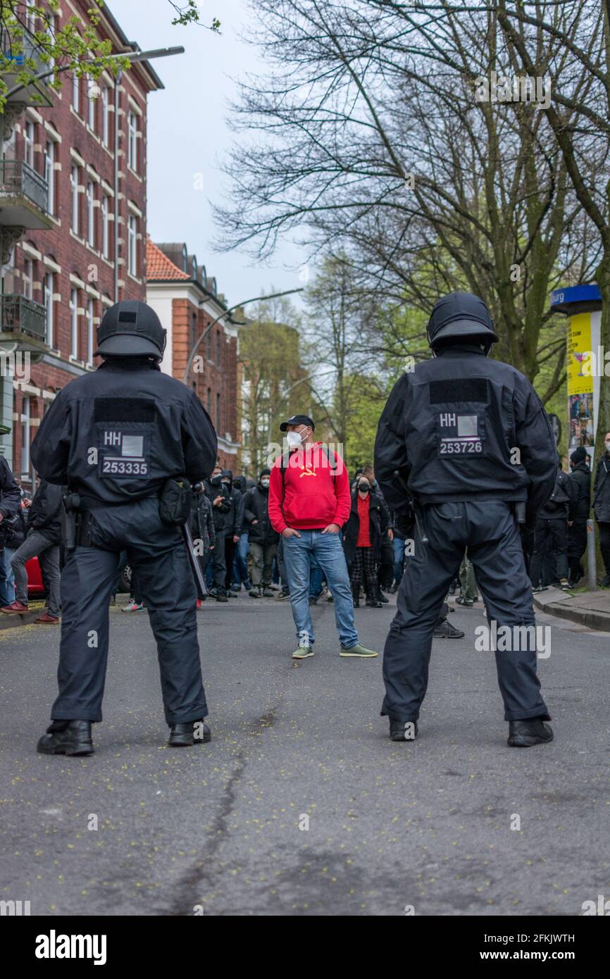 Hambourg, Allemagne - 1er mai 2021 : manifestant de gauche avec un marteau socialiste communiste et un pull à capuche à faucille face à la police anti-émeute pendant la manifestation Banque D'Images