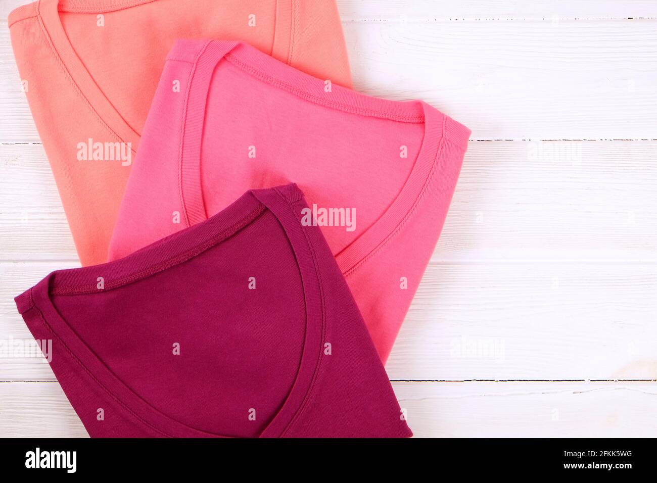 Pile de t-shirts colorés à col en V parfaitement pliés sur fond blanc de table en bois texturé. Pile de chemises et de chandails aux couleurs pastel différentes. Arrière Banque D'Images