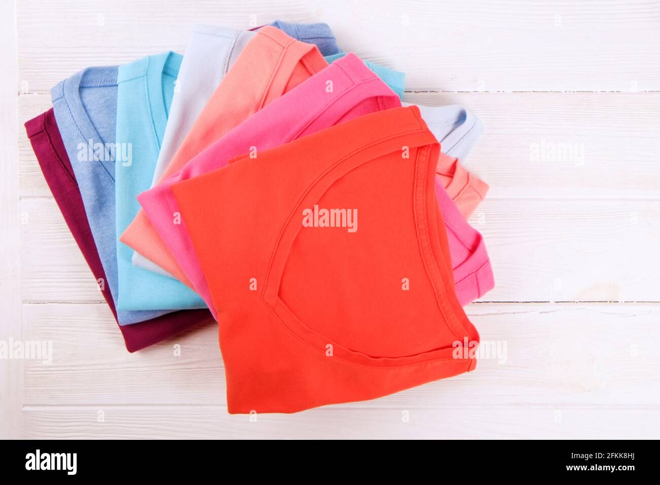 Pile de t-shirts colorés à col en V parfaitement pliés sur fond blanc de table en bois texturé. Pile de chemises et de chandails aux couleurs pastel différentes. Arrière Banque D'Images