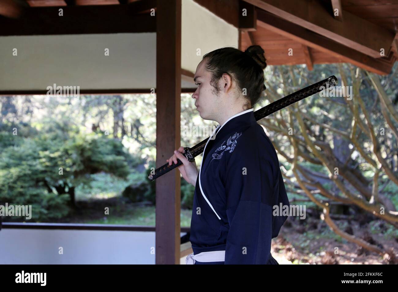 Homme en costume de samouraï se tient avec katana sur son épaule dans une maison de jardin japonaise. Saison des cerisiers en fleurs dans le jardin botanique de Moscou Banque D'Images