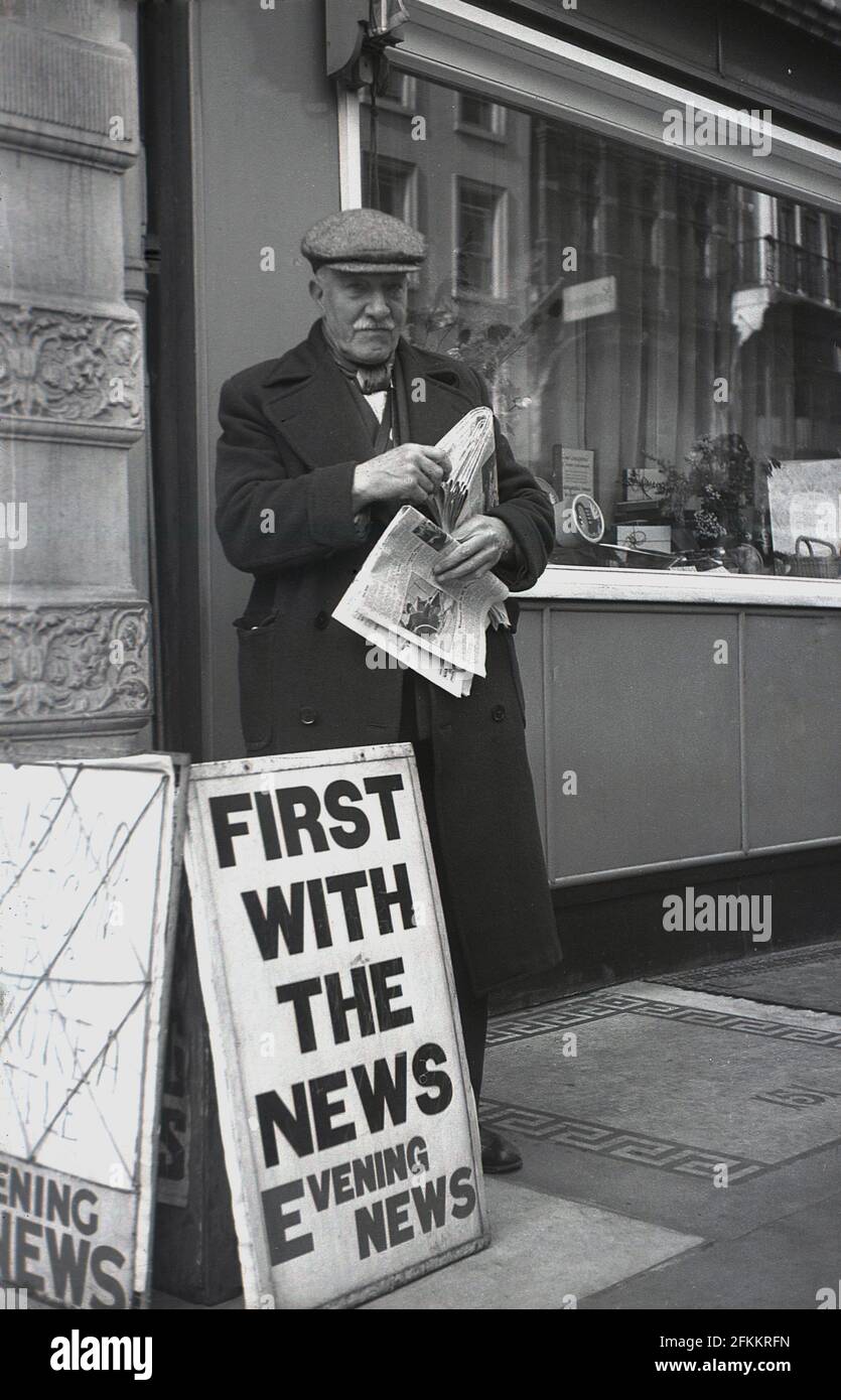 Années 1950, historique, un vieux vendeur de journaux, en manteau et en tissu de casquette debout à l'extérieur sur un pavé vendant le Evening News, Londres, Angleterre, Royaume-Uni. Banque D'Images