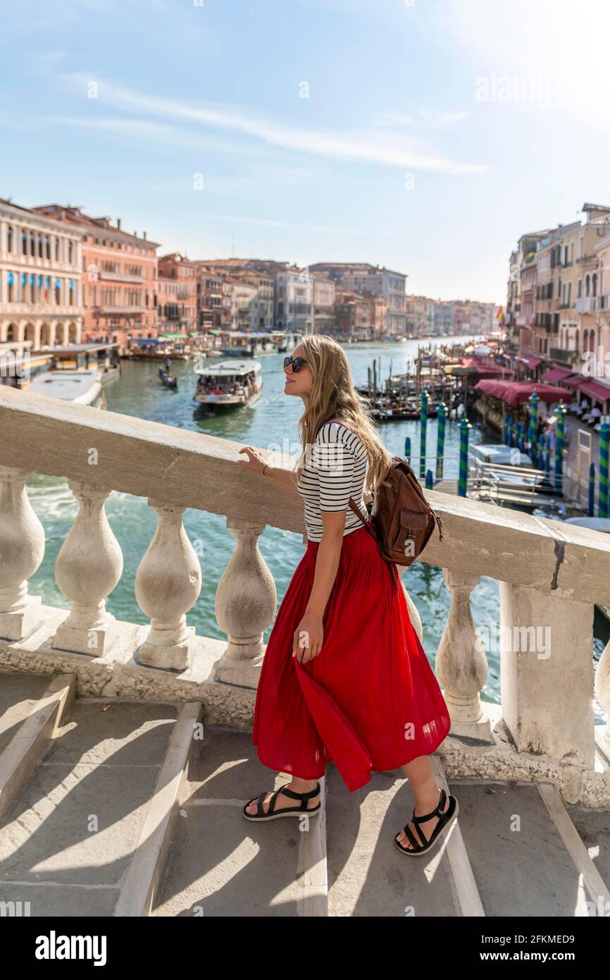 Une jeune femme à jupe rouge se promène sur un pont au Grand Canal, au Pont du Rialto, à Venise, en Vénétie, en Italie Banque D'Images
