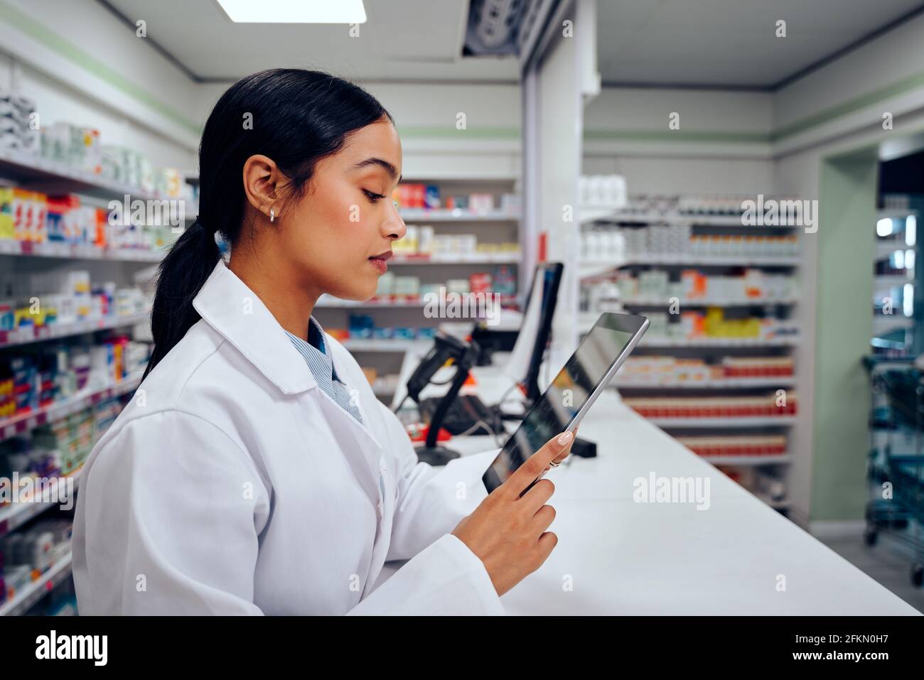 Jeune femme travaillant dans un chimiste utilisant une tablette numérique debout derrière compteur Banque D'Images