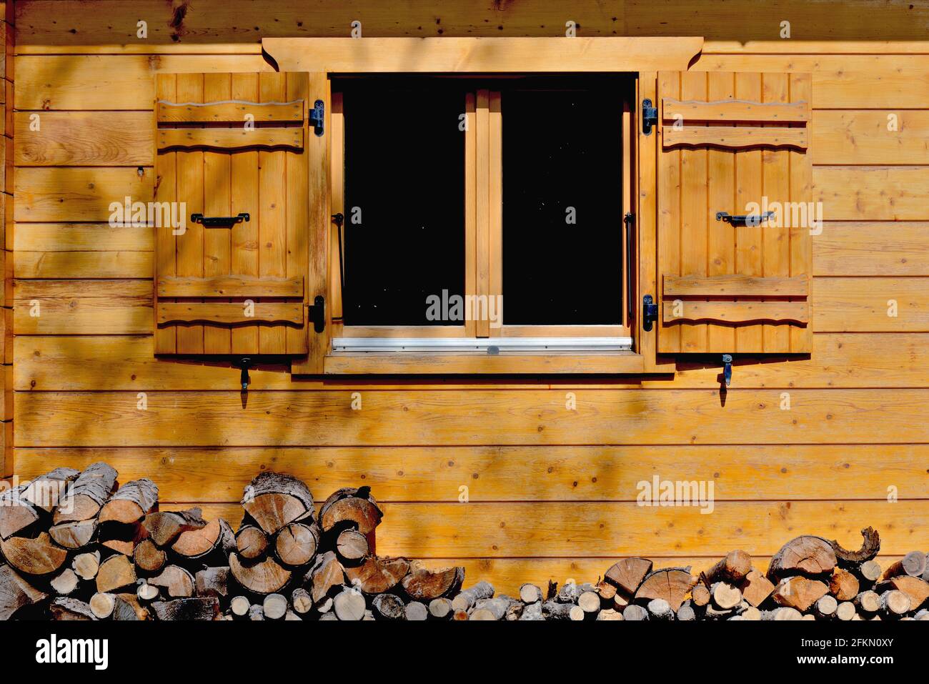 façade en bois avec une fenêtre et des volets ouverts d'un chalet alpin et bûches Banque D'Images