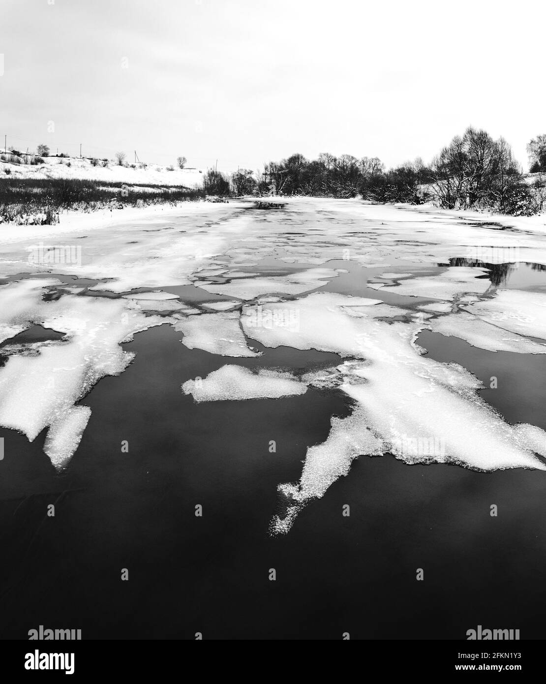 Paysage rural panoramique noir et blanc d'hiver ou de printemps avec flottant sur des morceaux de glace fondue à la surface de l'eau Banque D'Images