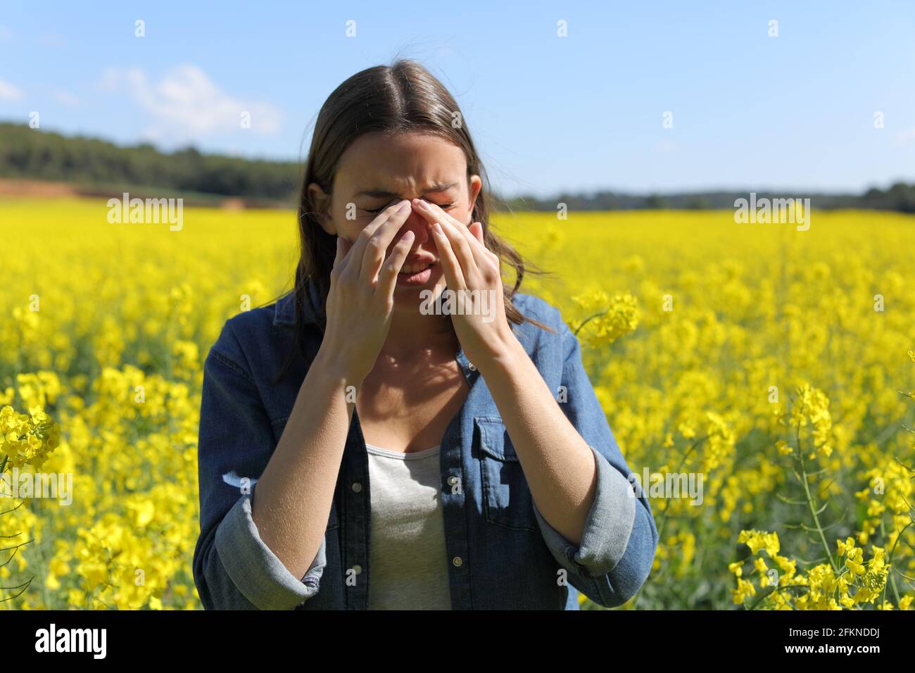 Femme allergique se grattant les yeux qui démangent au printemps en a champ à fleurs jaunes Banque D'Images
