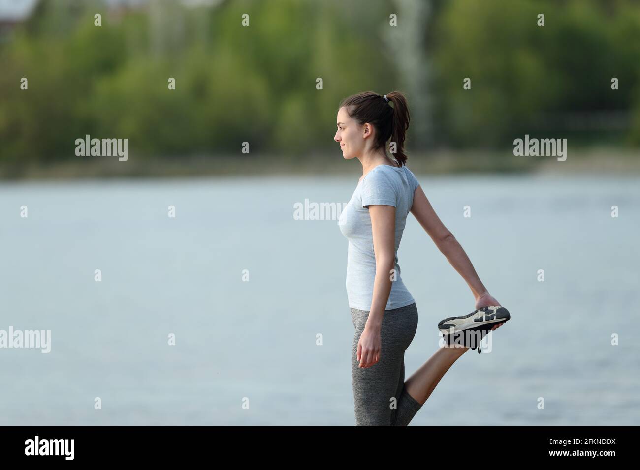 Vue latérale d'une sportswoman qui s'étire la jambe après le sport dans un lac Banque D'Images