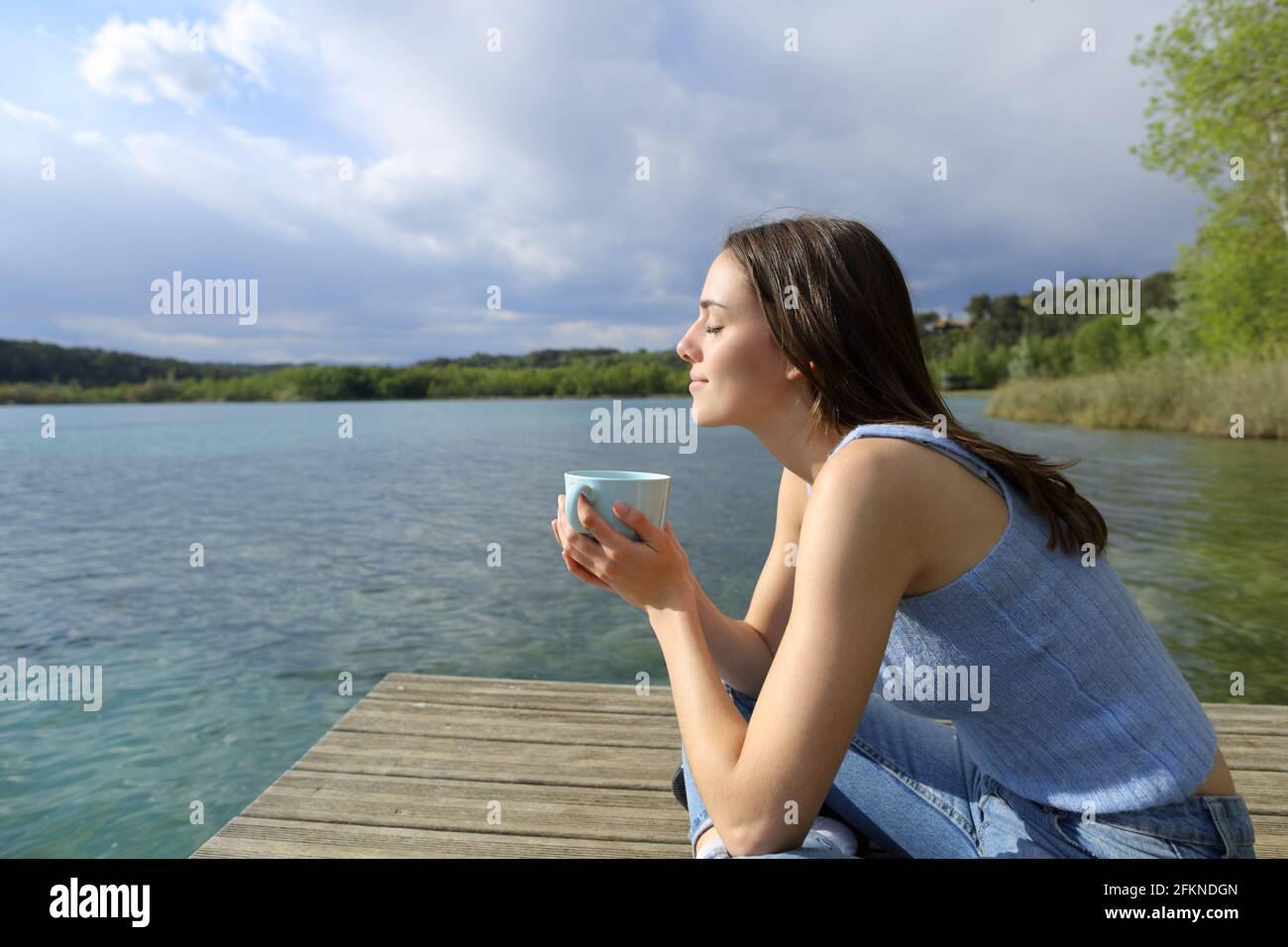 Profil d'une femme qui se détend en buvant du café dans un lac jetée Banque D'Images