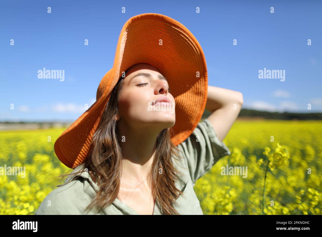Femme satisfaite avec orange pamela respirer de l'air frais dans un champ à fleurs jaunes Banque D'Images