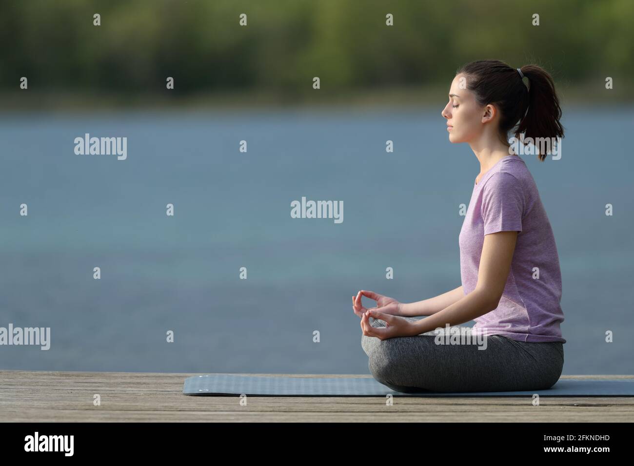 Profil d'un yogi pratiquant le yoga dans un quai à côté un lac Banque D'Images