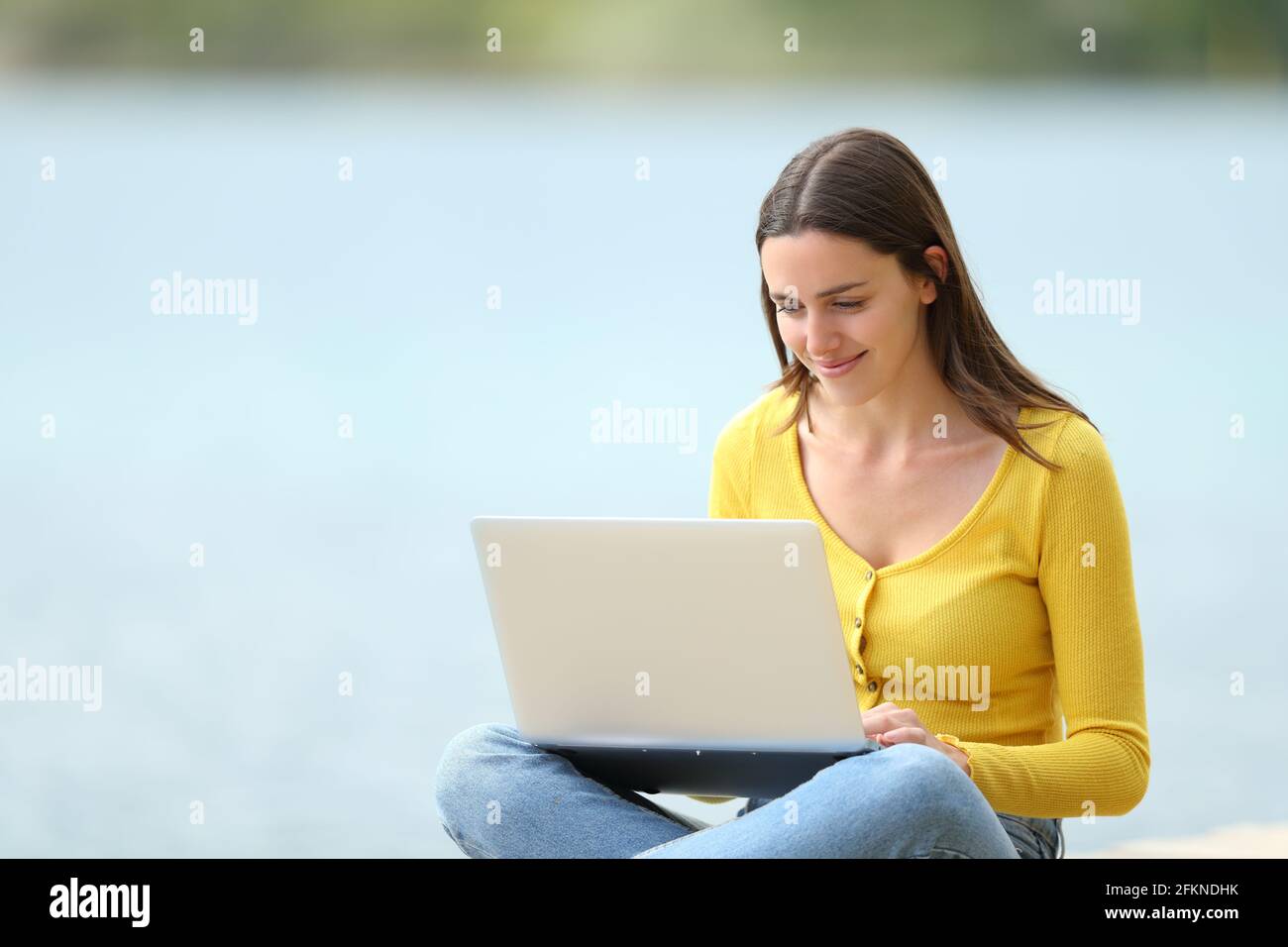 Une femme heureuse utilisant un ordinateur portable assis à côté d'un lac Banque D'Images