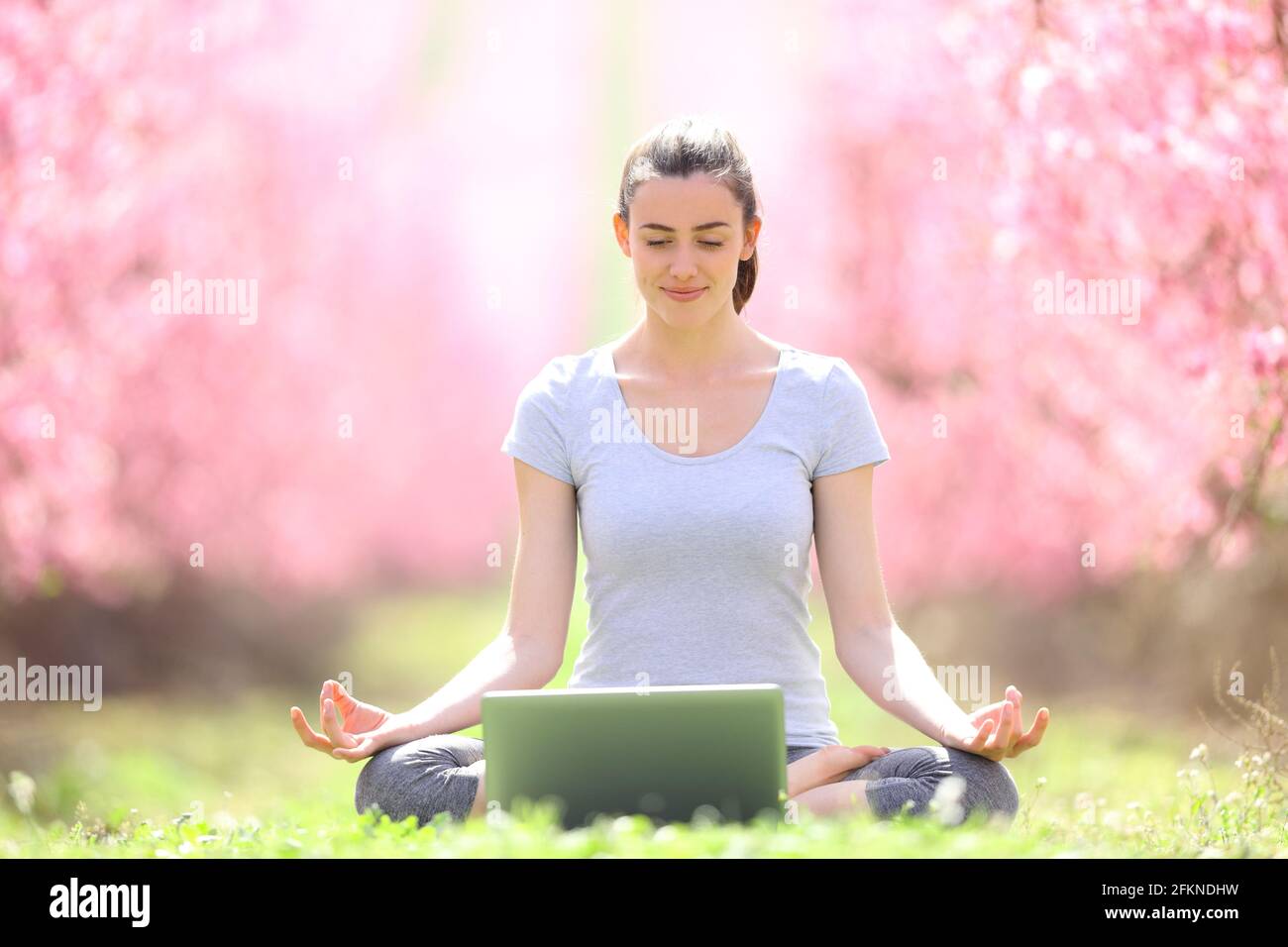 Vue de face d'un Happy yogi e-learning yoga avec un pc portable dans un champ au printemps Banque D'Images