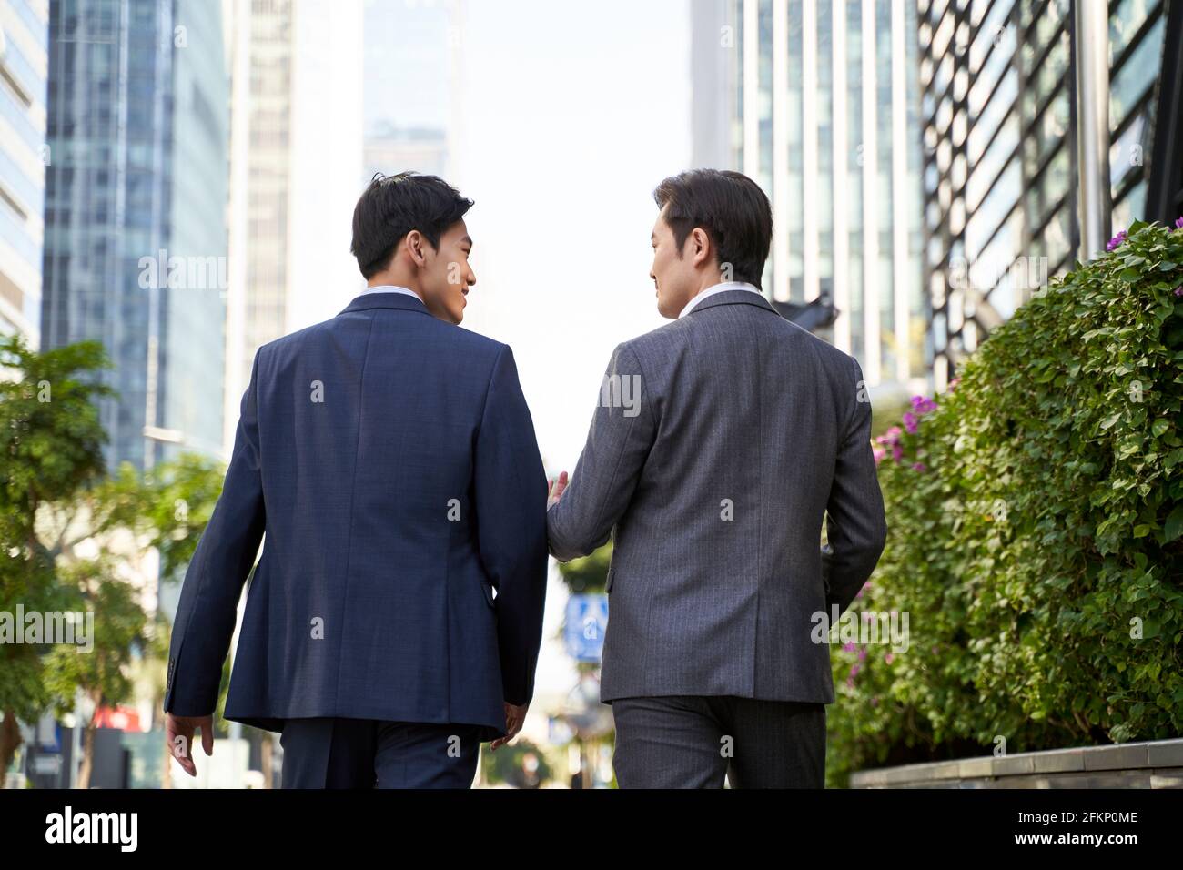 vue arrière de deux cadres d'entreprise asiatiques discutant des affaires pendant promenade dans la rue dans le centre-ville moderne Banque D'Images