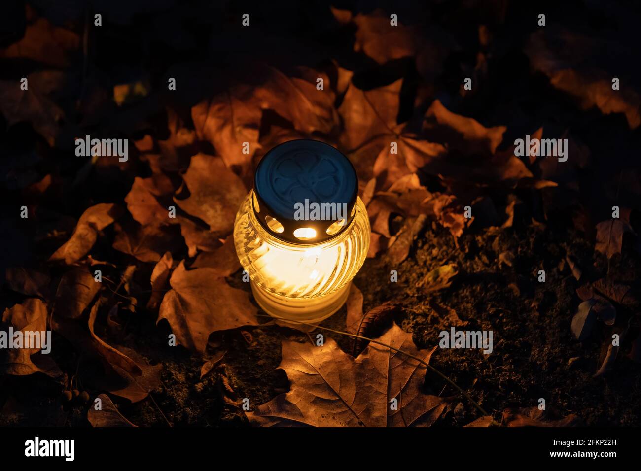 Une seule bougie au sol la nuit, entourée de feuilles d'automne. Banque D'Images