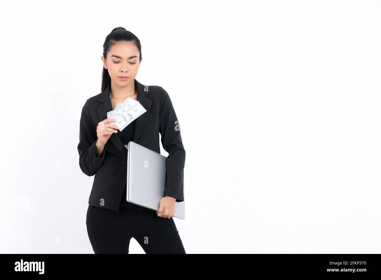 Portrait femme d'affaires portant un costume noir tenant des billets d'argent tout en étant debout avec ordinateur portable isolé sur fond blanc. Banque D'Images