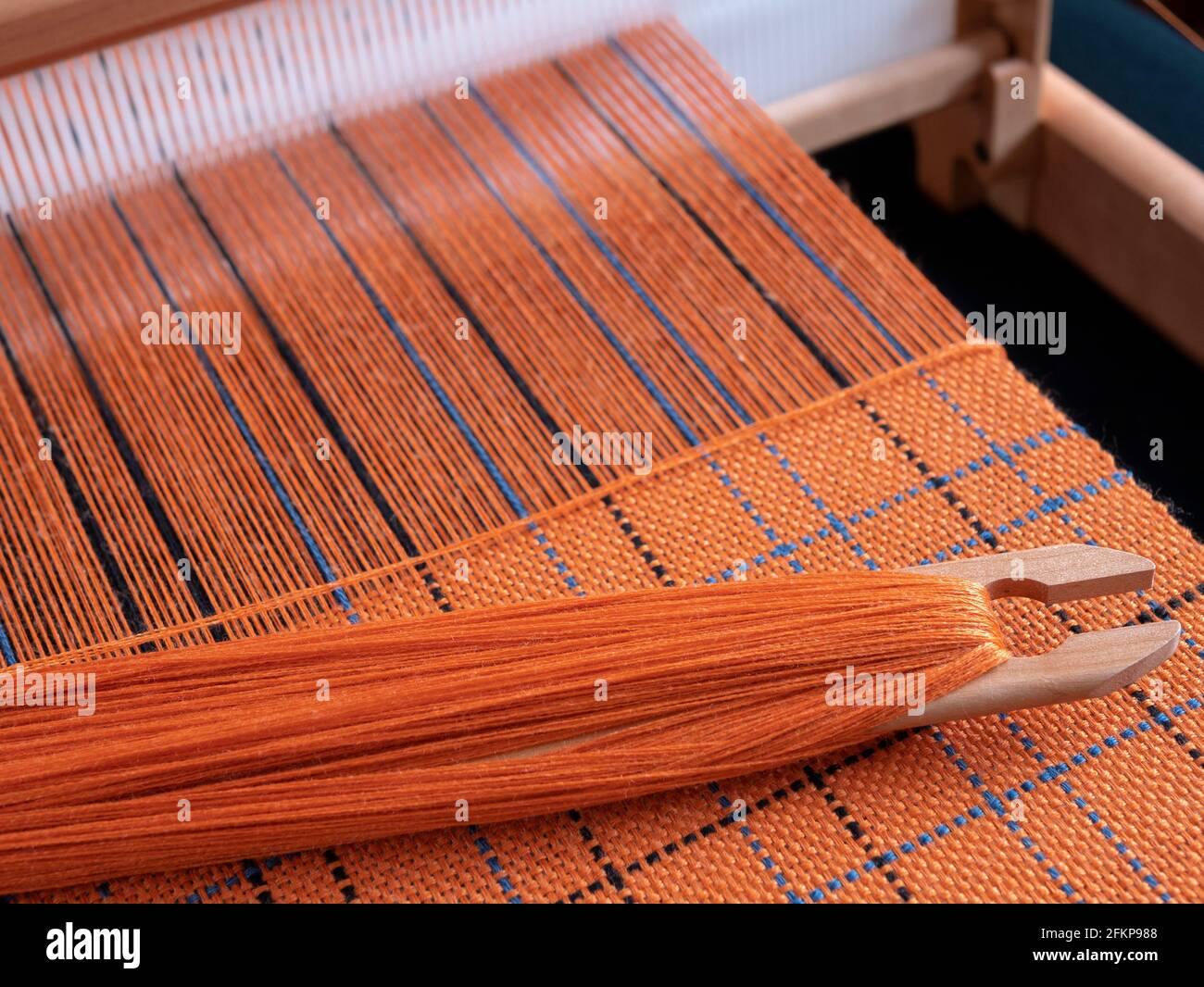 Métier à tisser en bois avec navette et textile orange tissé avec motif à rayures. Concept de tissage à la main Banque D'Images