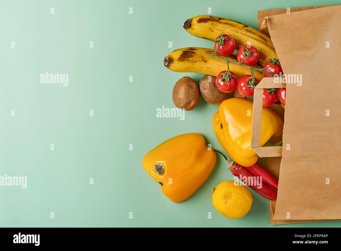 Assortiment de poivre frais, Chili, bananes, tomates cerises, citron et kiwi dans un sac de papier artisanal sur fond vert. Des légumes biologiques et branchés et Banque D'Images