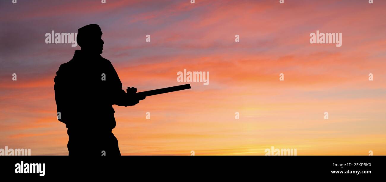 Silhouette d'un chasseur avec une arme à feu sur le fond du ciel du coucher de soleil Banque D'Images