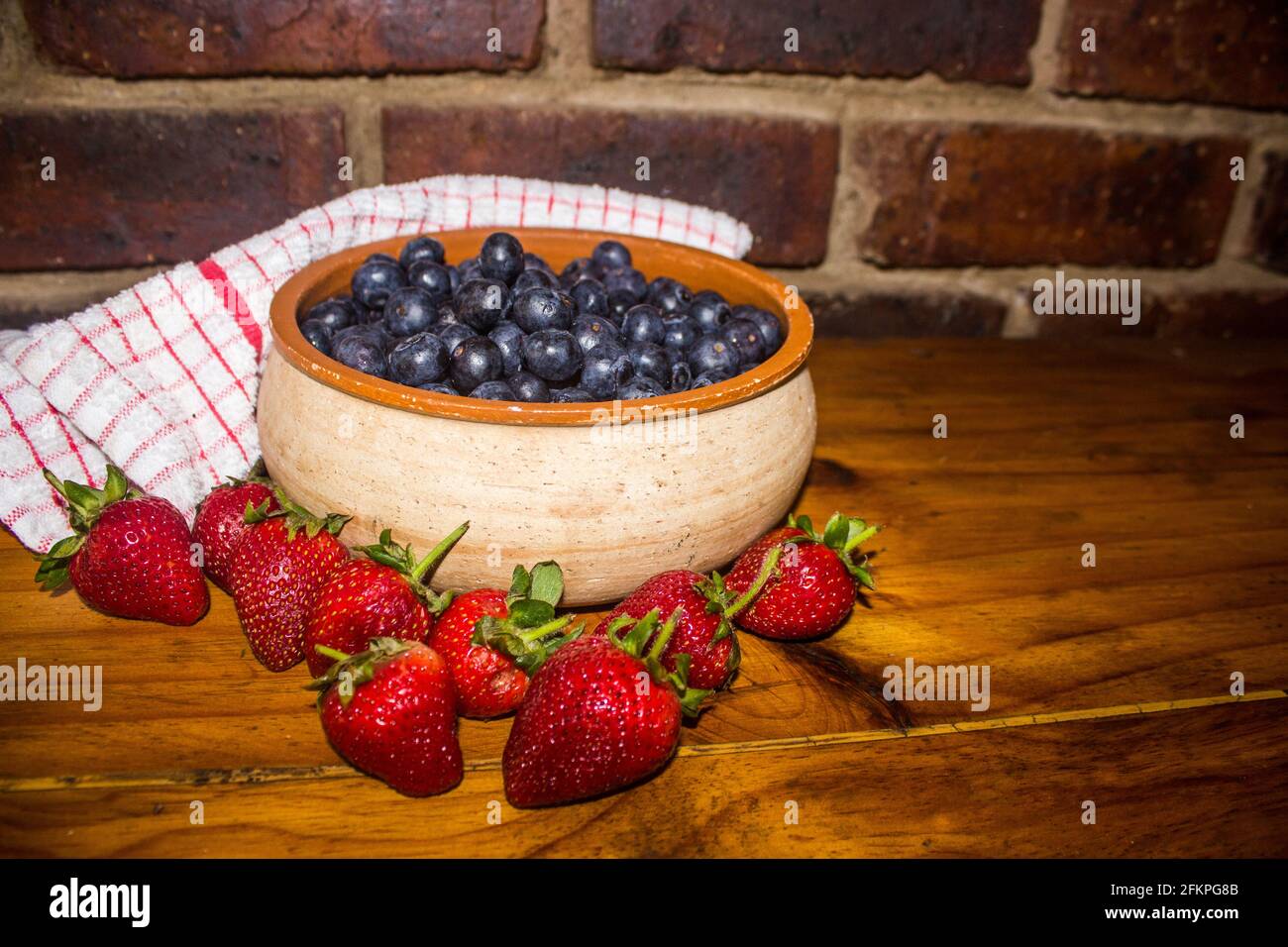 Une vie encore composée d'un bol de poterie rustique rempli de grands bleuets succulents, entouré de fraises Banque D'Images