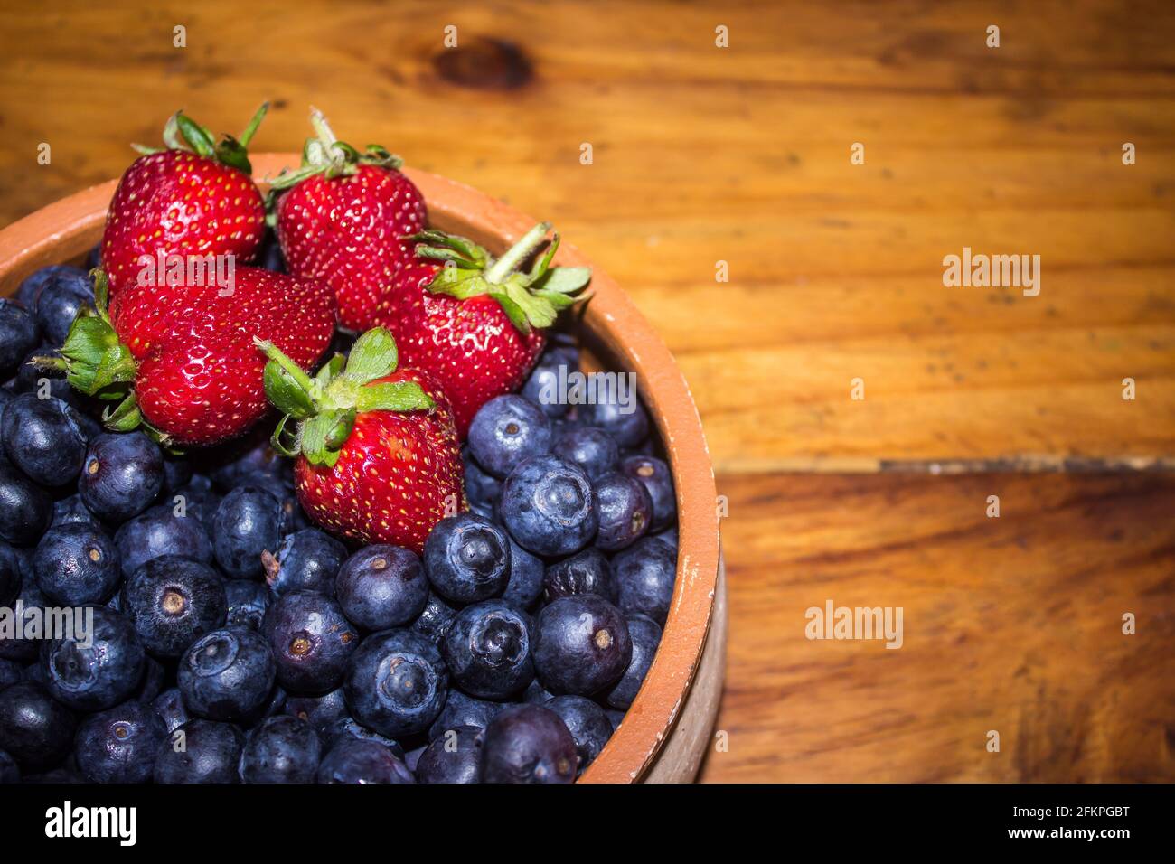 Un bol rustique avec quelques fraises rouges brillantes, sur une grande  quantité de bleuets de couleur indigo Photo Stock - Alamy