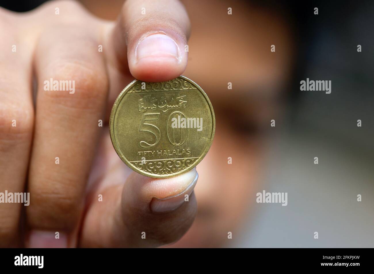 Main d'enfant asiatique tenant une cinquante pièces de monnaie à Riyal halalas, l'argent de l'Arabie Saoudite, foyer choisi Banque D'Images