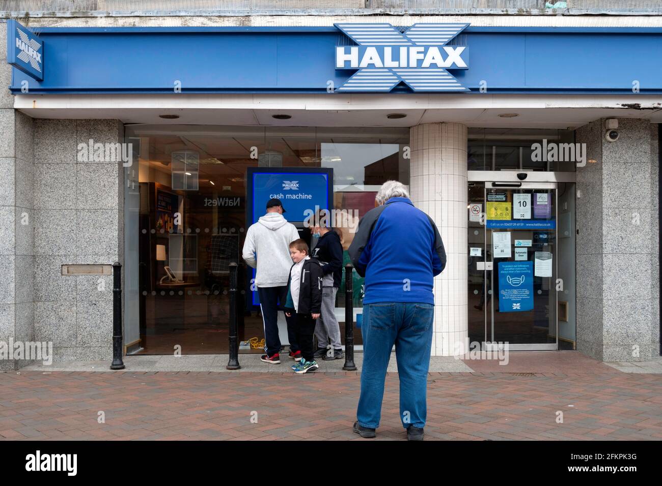Un groupe familial qui retire de l'argent d'un guichet automatique de la Halifax Bank Ou Cash machine pendant qu'un client de sexe masculin se démène Banque D'Images