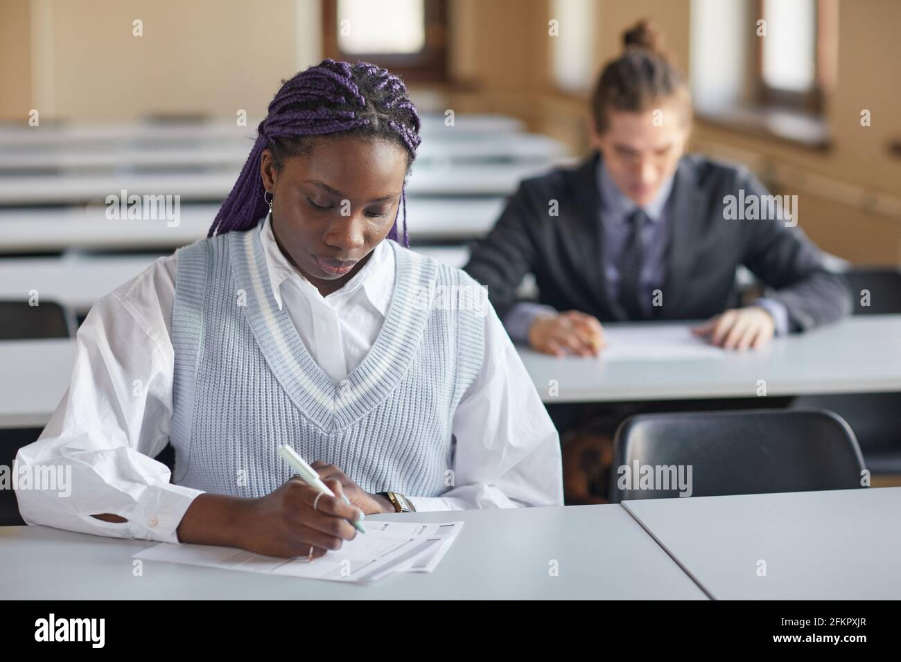Portrait d'une jeune femme afro-américaine portant l'uniforme scolaire tout en prenant l'examen dans l'auditorium d'université, l'espace de copie Banque D'Images