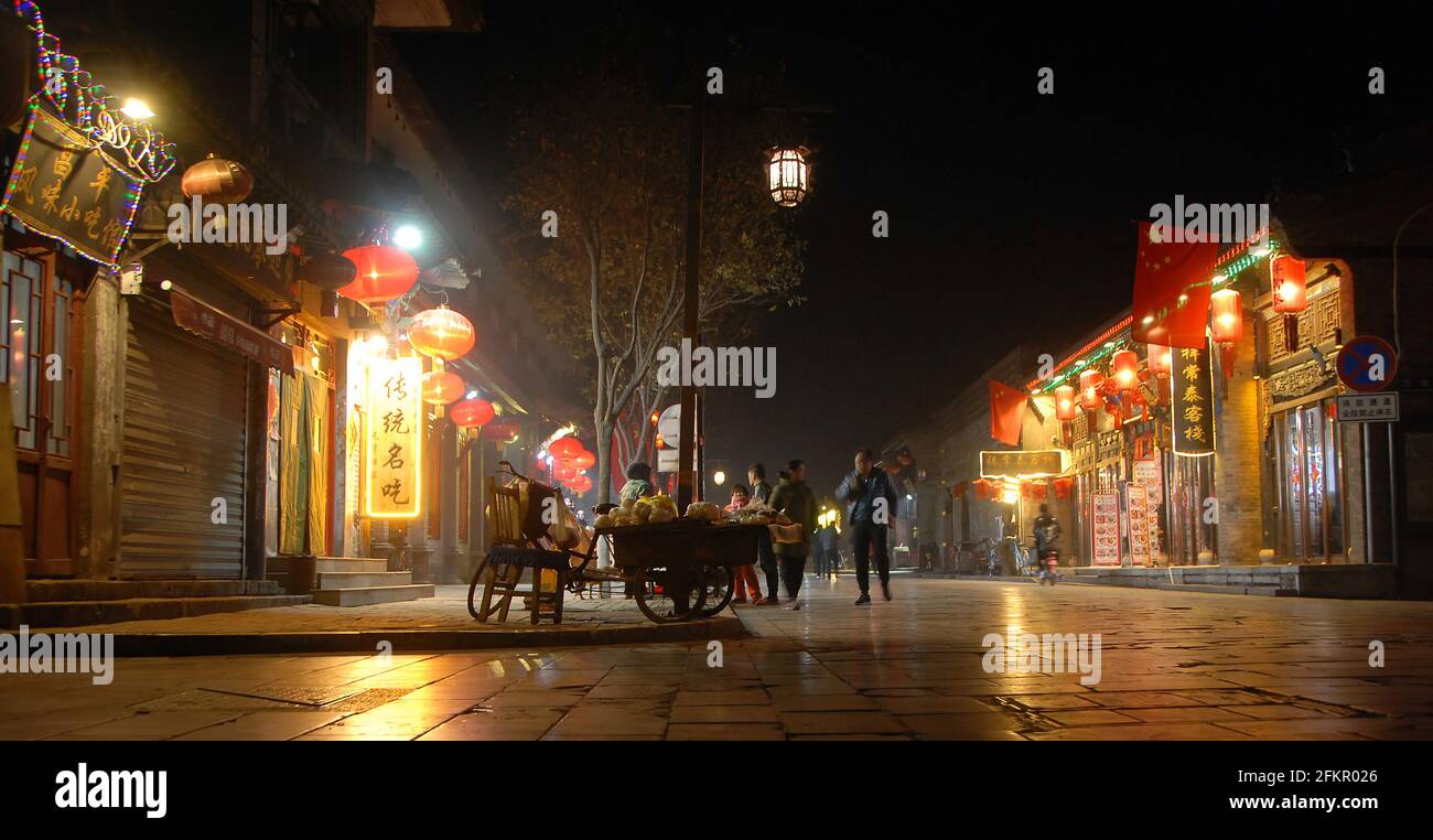 Pingyao dans la province du Shanxi, Chine : scène de rue à Pingyao la nuit avec lumières de la ville, lanternes rouges et drapeaux chinois. Les gens qui marchent dans la vieille ville. Banque D'Images