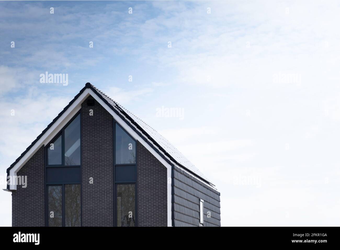 Panneaux solaires montés sur le toit d'une nouvelle maison moderne dans une rue aux pays-Bas avec soleil et ciel bleu nuageux. Énergie durable Banque D'Images