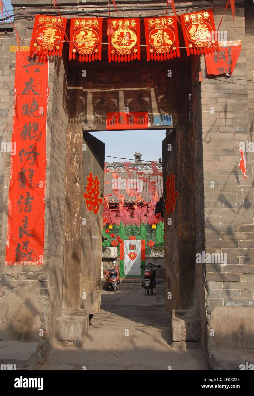 Vue sur une cour à Pingyao, province du Shanxi, Chine avec l'entrée décorée de bannières rouges et de textes chinois. Banque D'Images