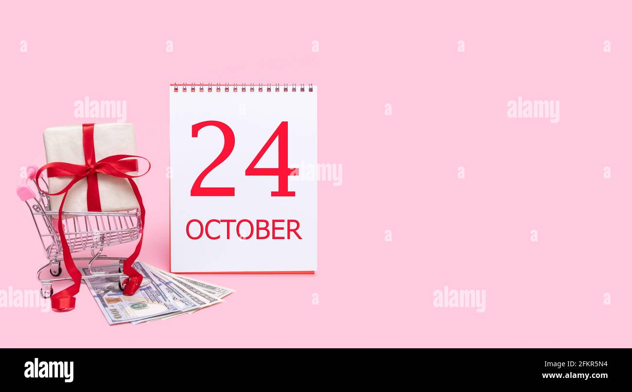 24 octobre. Une boîte cadeau dans un chariot, des dollars et un calendrier avec la date du 24 octobre sur fond rose. Automne mois, jour de t Banque D'Images