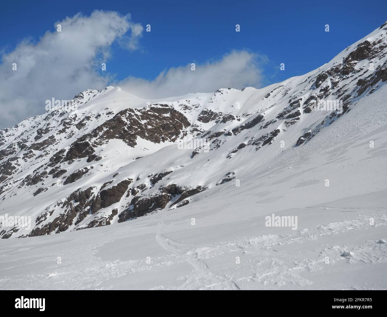 Hiverner dans les montagnes rocheuses couvertes de neige contre le bleu ciel avec petits nuages Banque D'Images