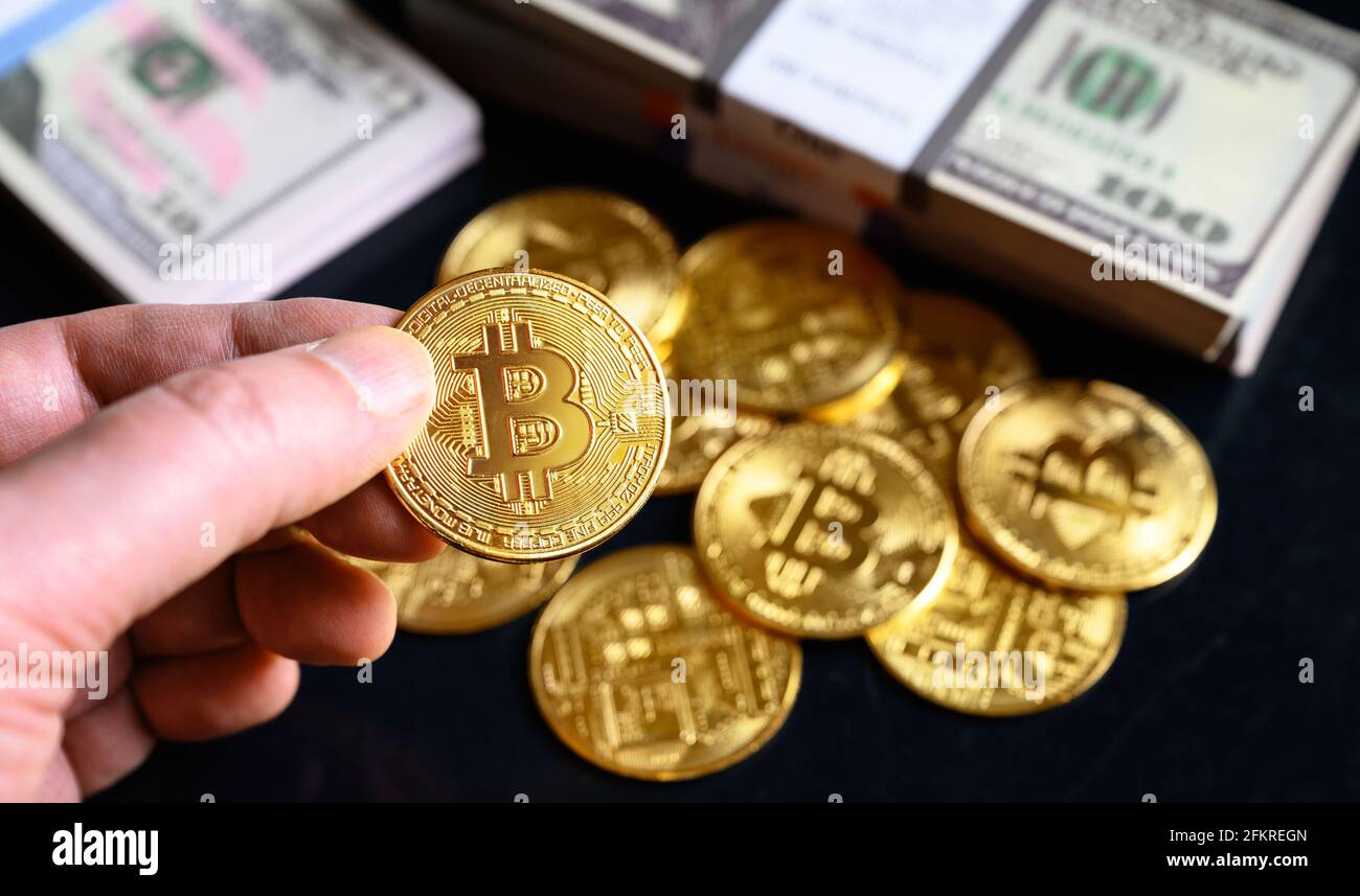 Bitcoin avec piles de dollars en espèces, crypto virtuel numérique bitcoin en monnaie (btc) et papier-monnaie. Une pièce de monnaie en forme de petit morceau d'or à la main sur fond d'argent. Concept Banque D'Images