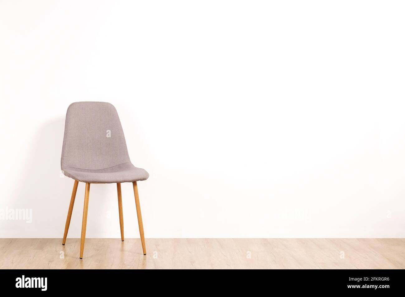 Chaise simple élégante de style loft grise debout seul sur un plancher en bois dans une pièce vide, grand fond de mur vierge. Grand espace de copie pour le texte. Un seul vaca Banque D'Images