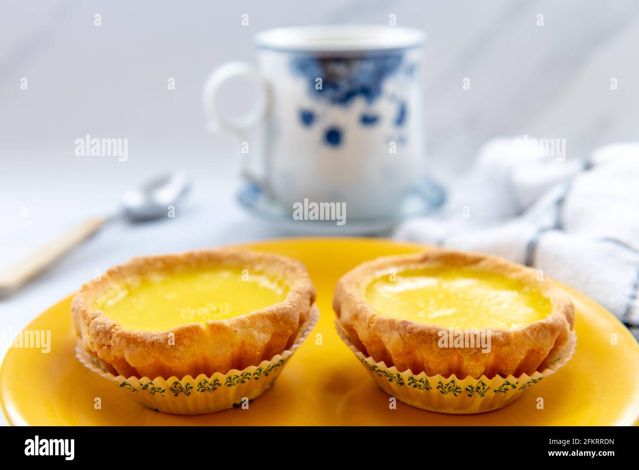 Tartes aux œufs sur une assiette jaune avec une tasse de thé. Banque D'Images