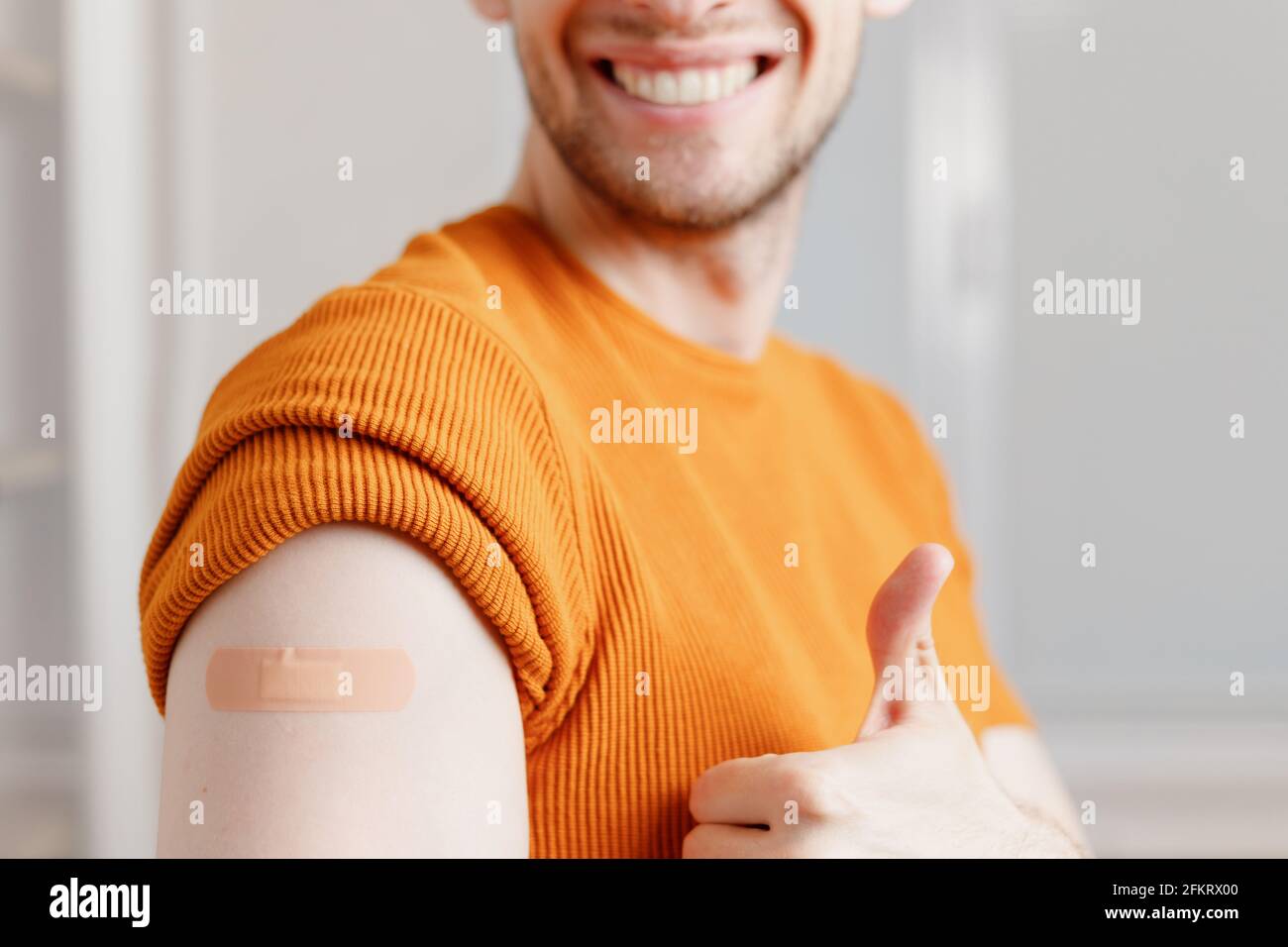 Jeune homme souriant avec pansement adhésif sur l'épaule montrant le pouce vers le haut geste après injection vaccin. Vue rognée en gros plan Banque D'Images