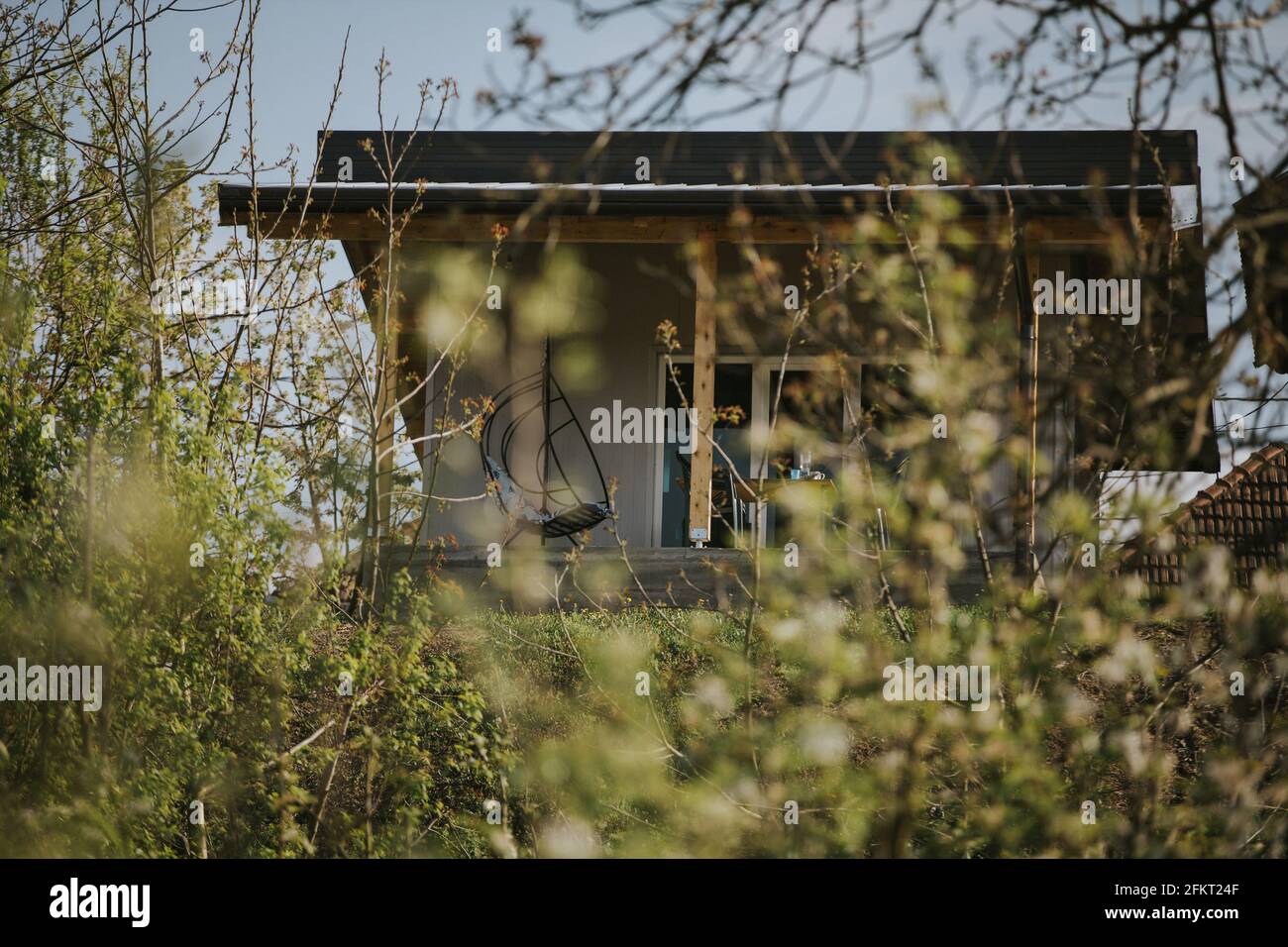 Maison moderne vue par des ouvertures entre les branches et les buissons, avec un fauteuil à oeufs sur le porche Banque D'Images