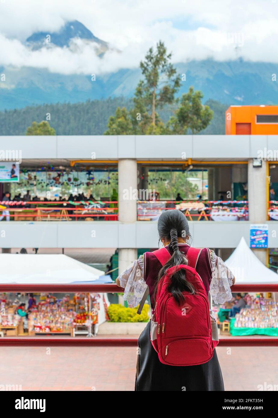 Jeune femme indigène Otavalo avec sac à dos d'école et des vêtements traditionnels dans le marché local moderne avec le volcan Imbabura en arrière-plan, Equateur. Banque D'Images