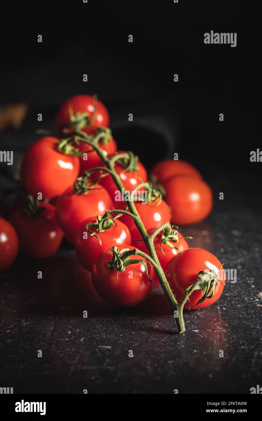 Tomates cerises rouges fraîches. Petites tomates sur branche sur table noire. Banque D'Images