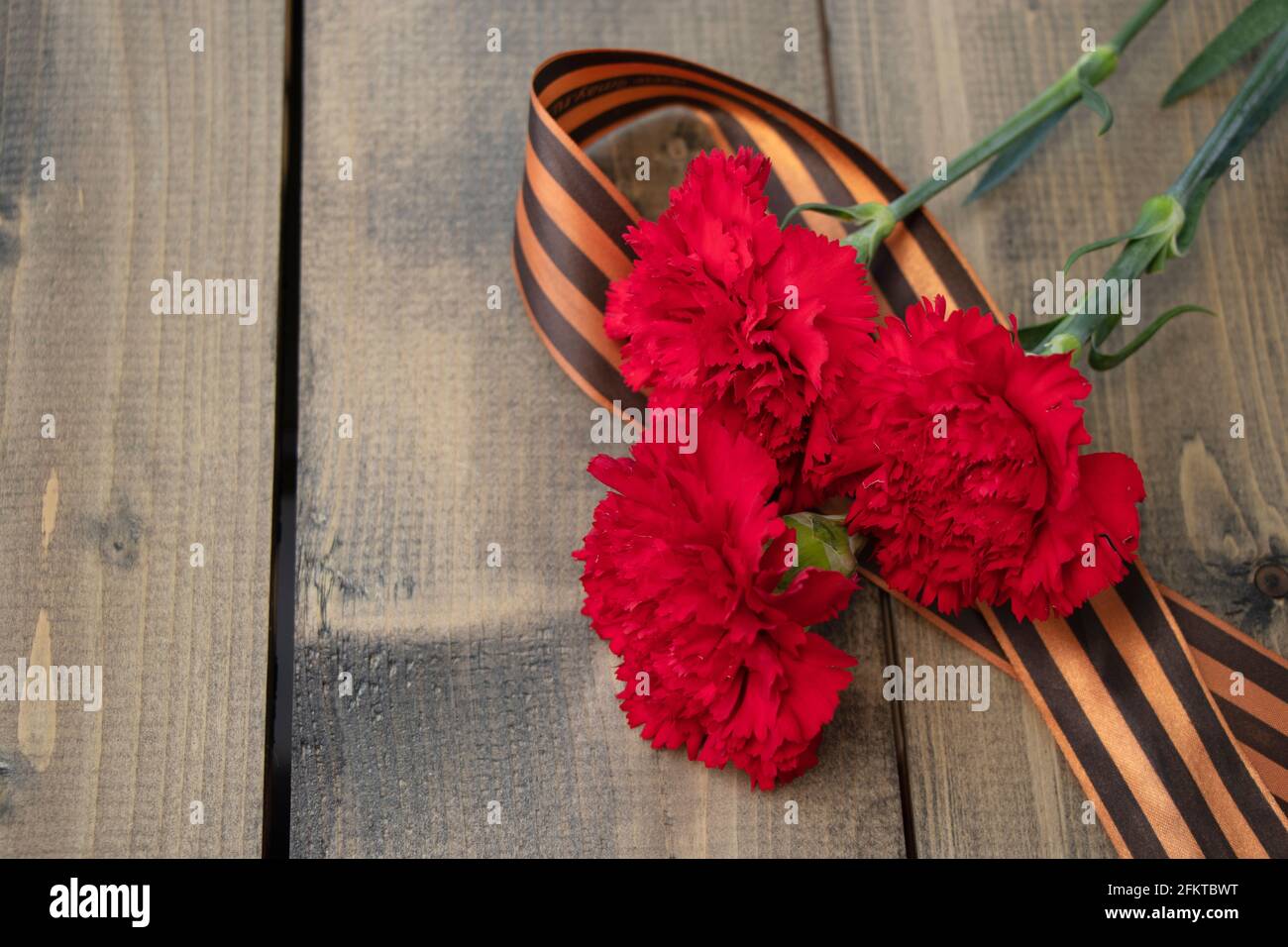 Bouquet d'œillets rouges avec un ruban de Saint-Georges sur fond de bois. Ruban de Georgievsk - symbole russe de la victoire et trois œillets rouges. Hol Banque D'Images