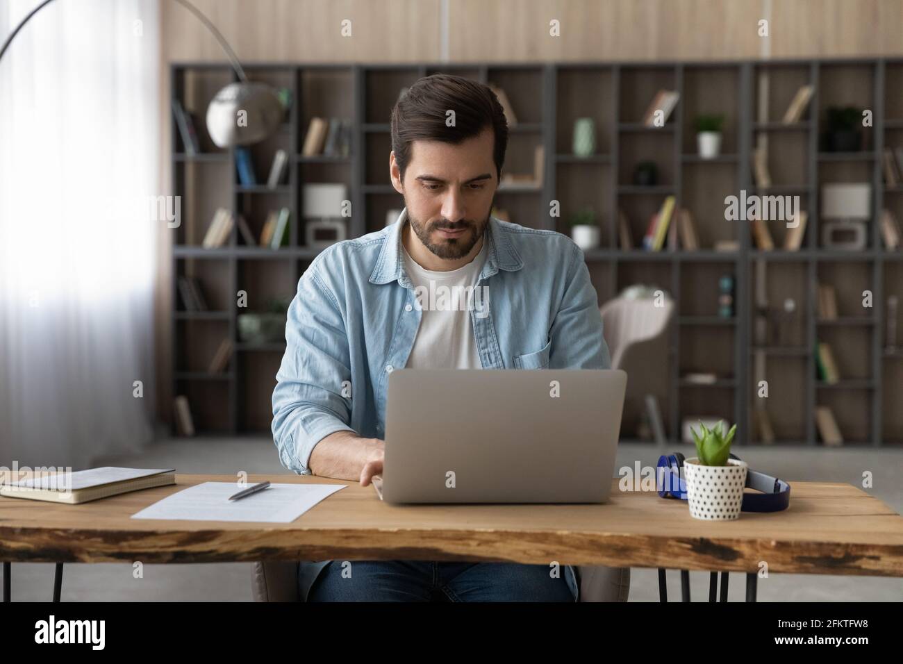 Homme d'affaires confiant travaillant sur un ordinateur portable en ligne, assis à un bureau en bois Banque D'Images
